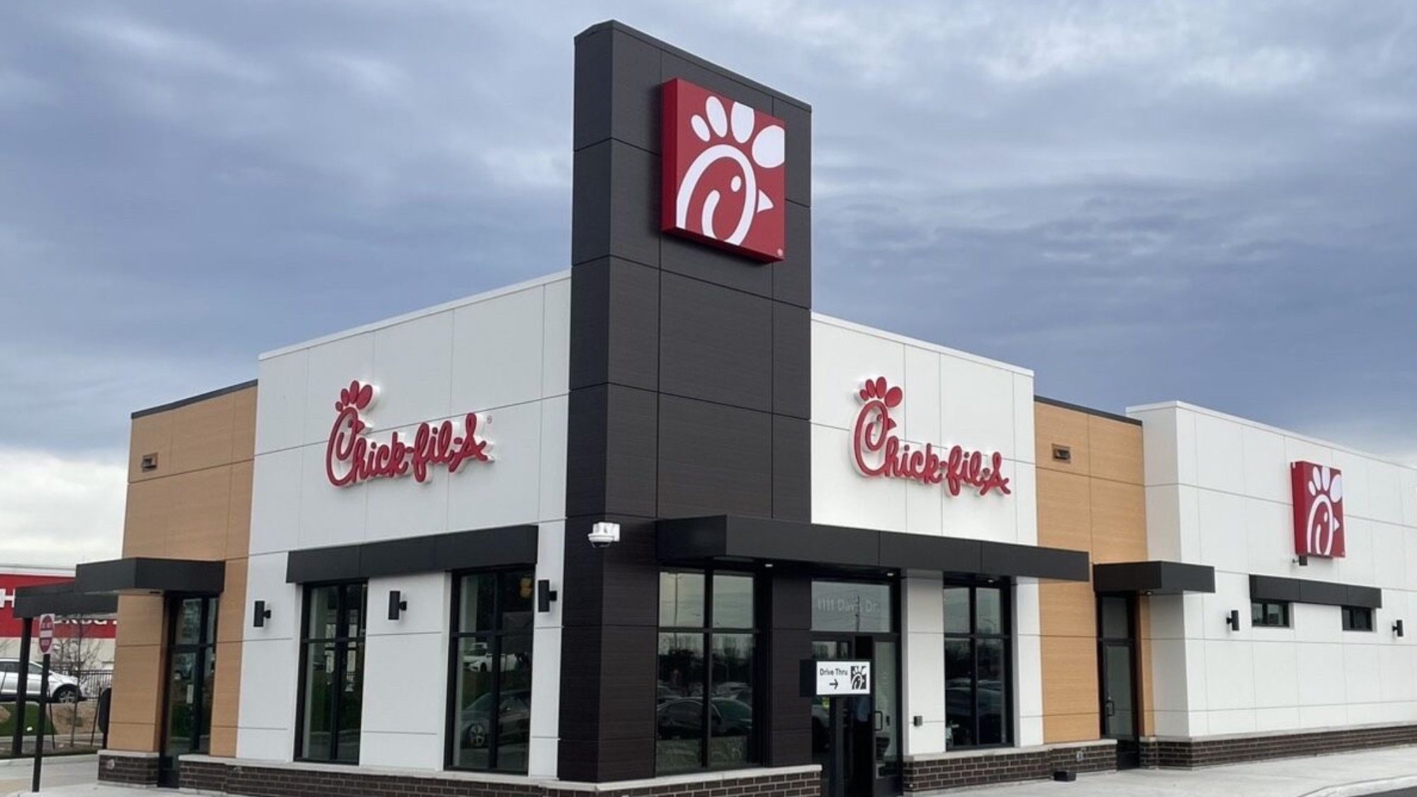 Exterior view of a Chick-fil-A restaurant with a red logo on a corner building under a cloudy sky.