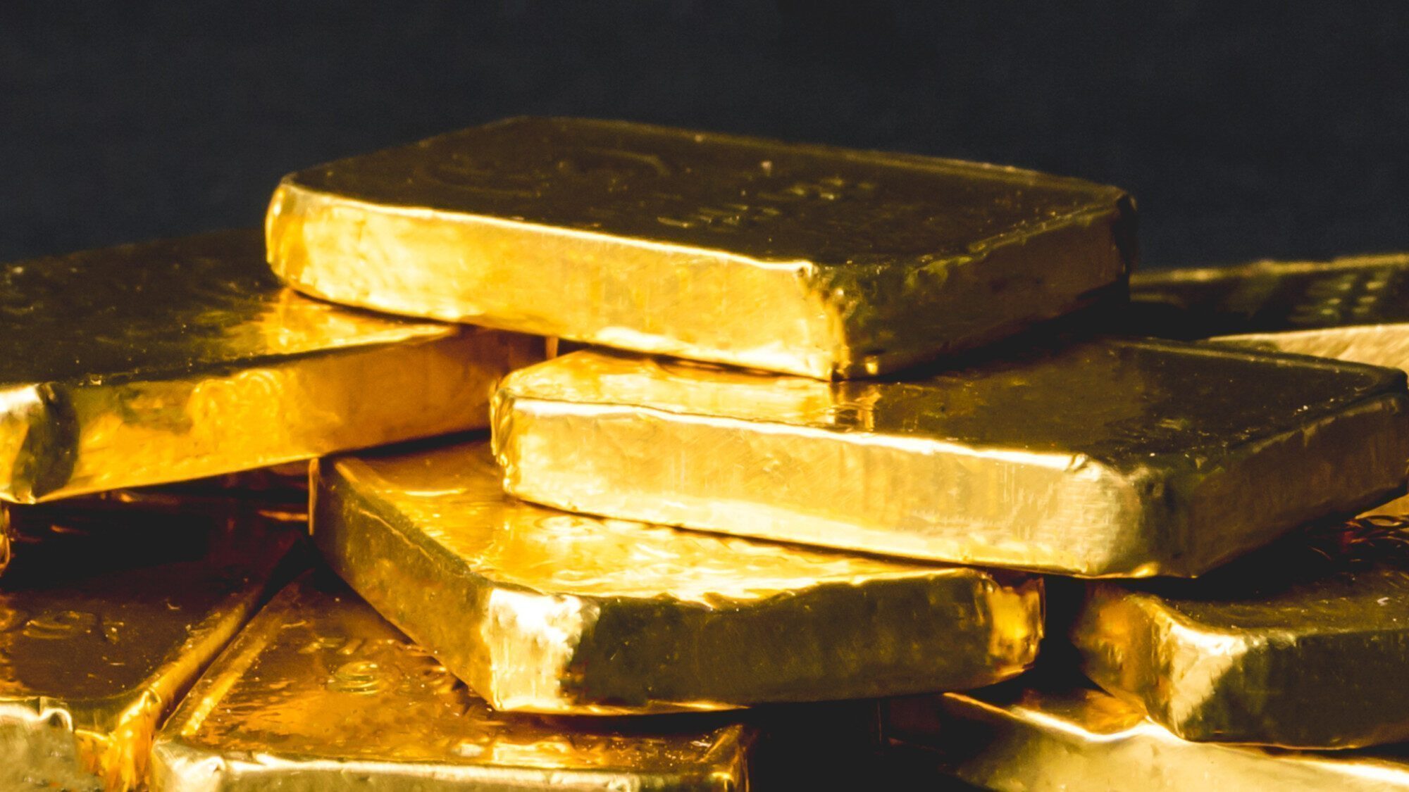 Several shiny gold bars are stacked unevenly against a dark background.