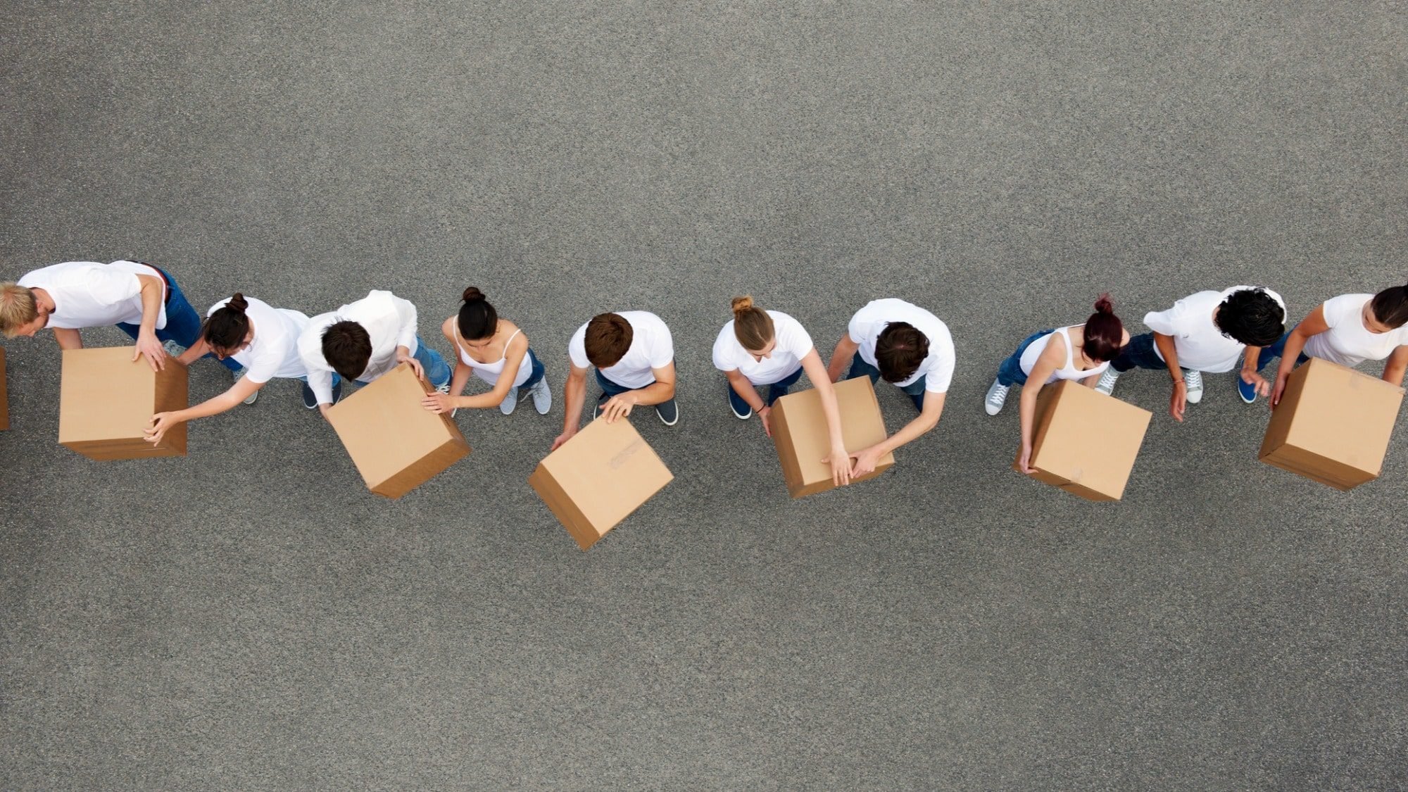 Aerial view of a group of people in white shirts implementing anti-counterfeiting measures by packing boxes in an organized line on a gray background.