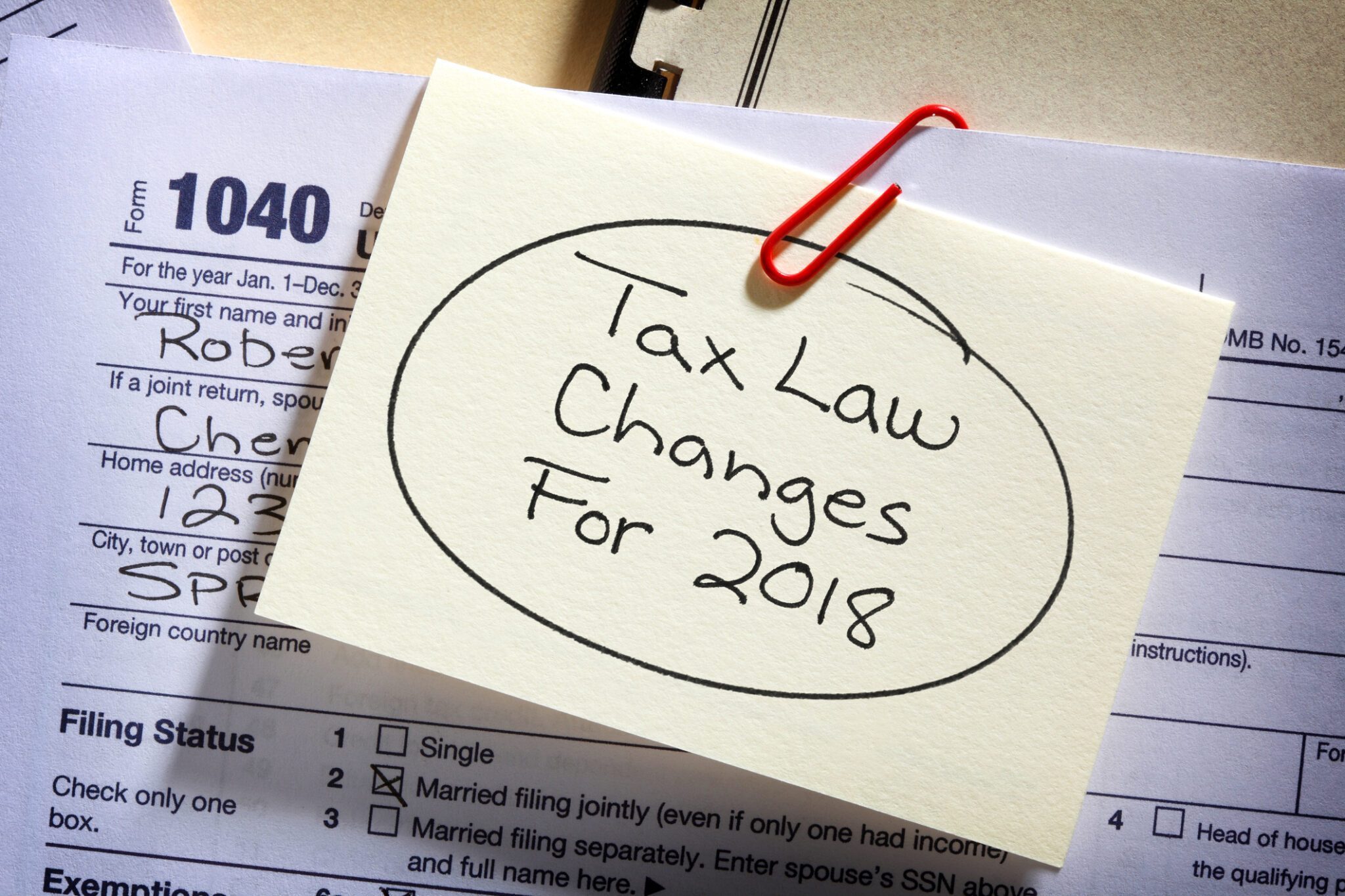 A yellow note is paper clipped to a 1040 tax form as a reminder of the new tax laws implemented for 2018.