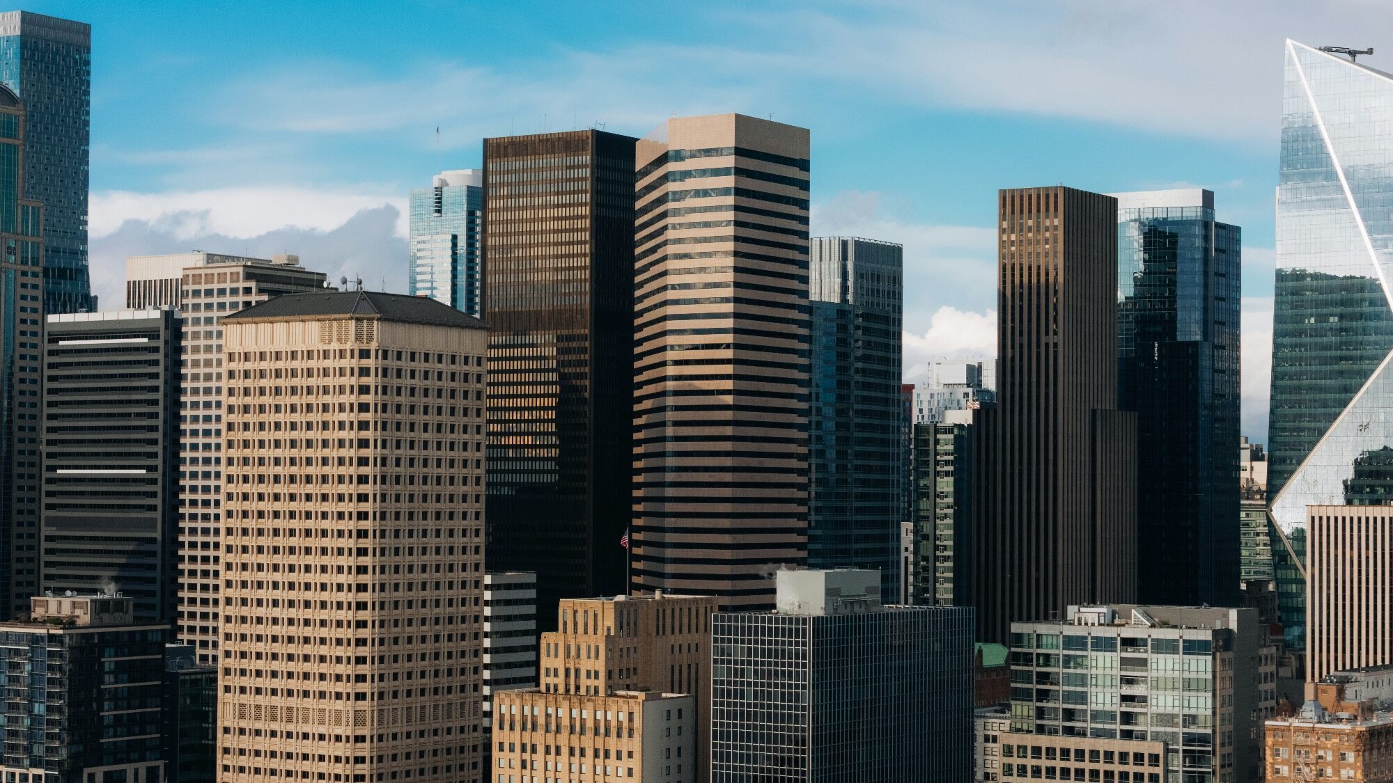 A cluster of modern high-rise office buildings with glass and concrete facades against a blue sky with some clouds.