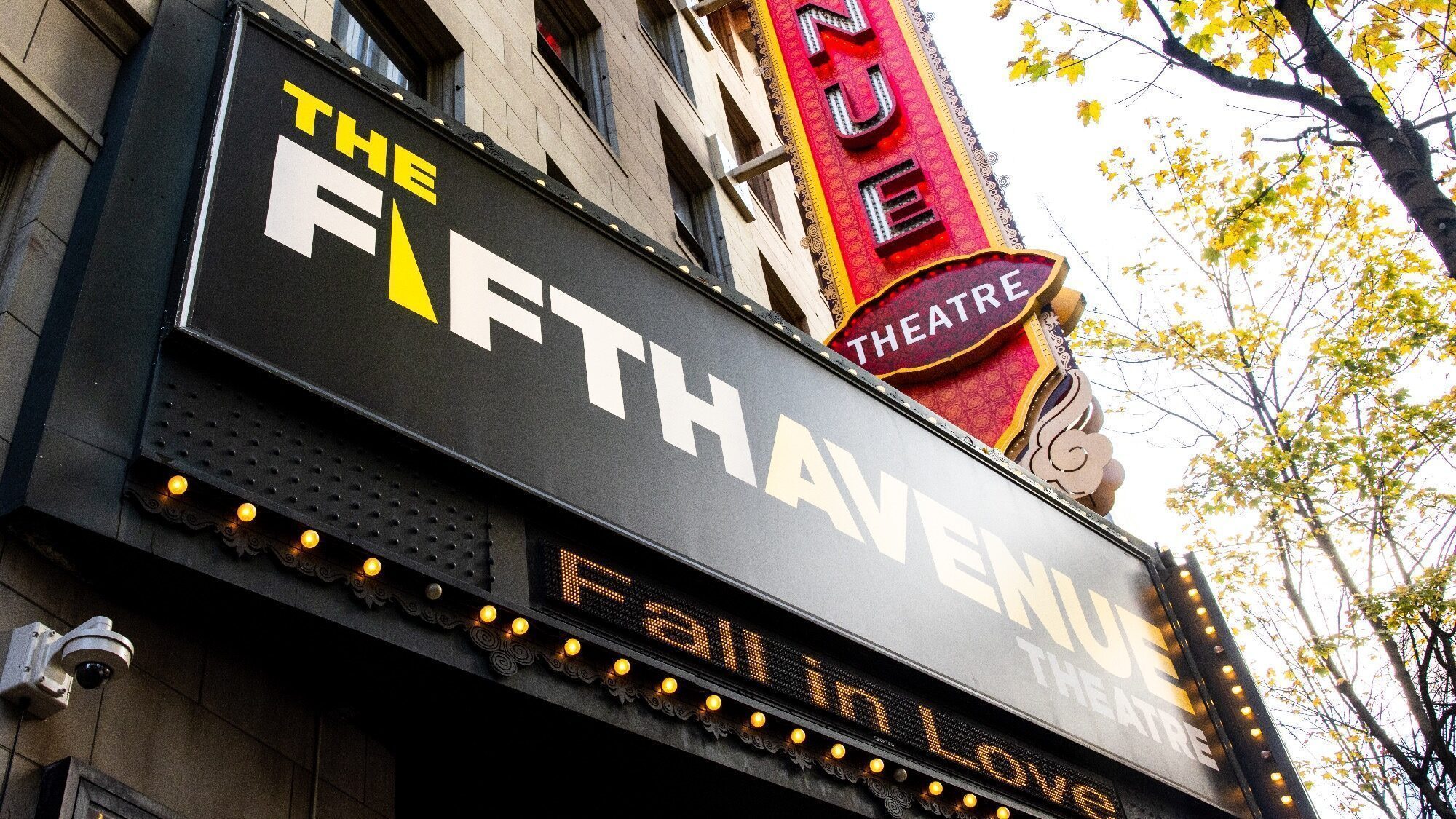 Marquee of The 5th Avenue Theatre with a red and white vertical sign on the side. The words "Fall in Love" are displayed on the lower part of the marquee.
