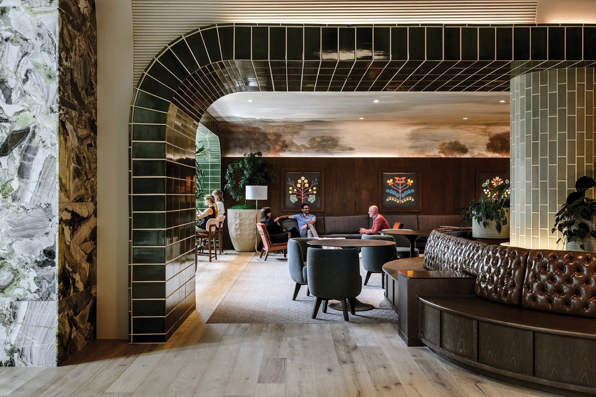 People sit in a modern, stylish lounge designed by architect Kyle Gaffney, featuring green tiled arches, wooden floors, and decorative wall panels, all engaged in lively conversation.