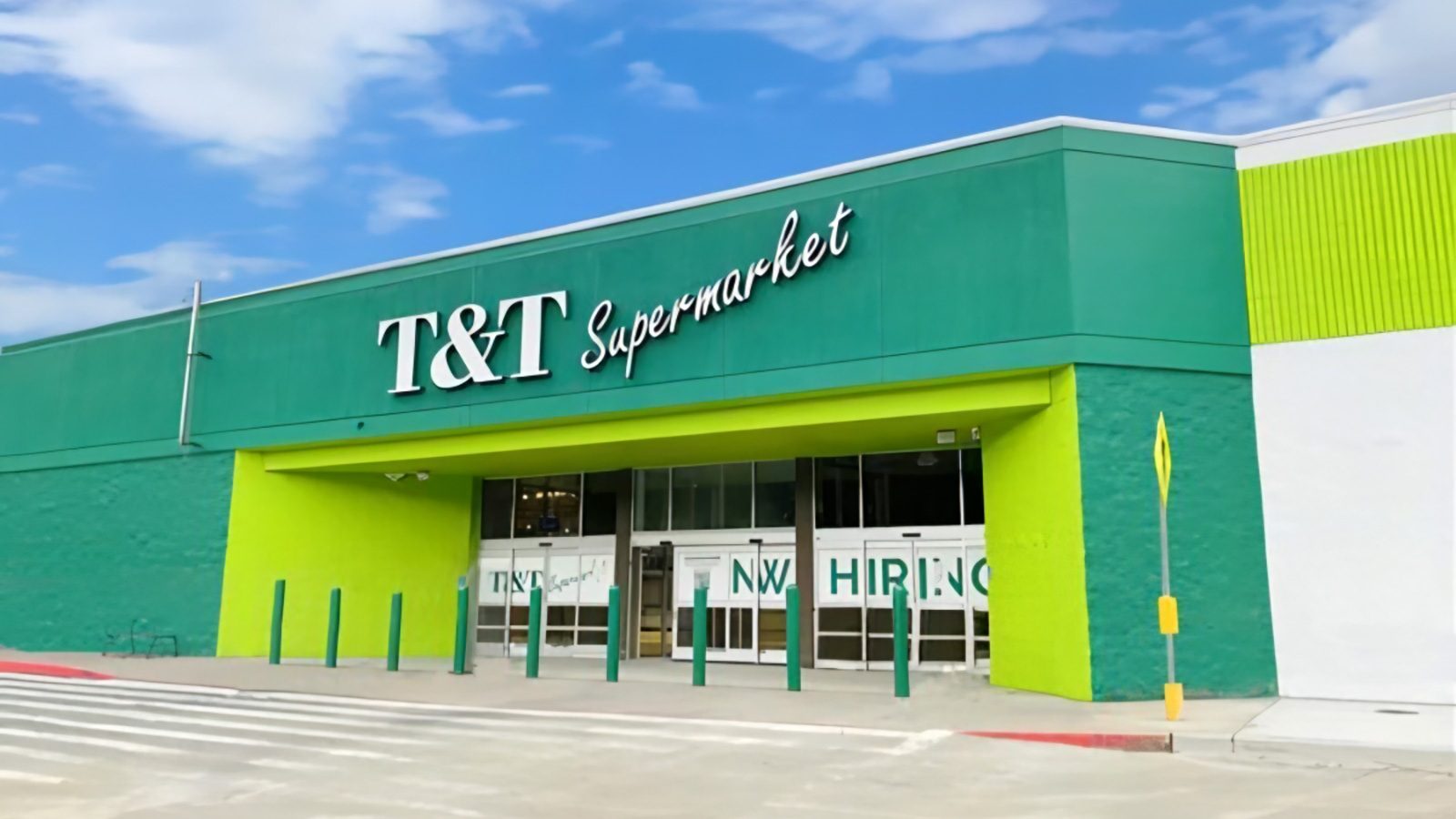 The exterior of T&T Supermarket, an Asian grocery chain, features green and white signage with large glass doors and windows. A "Now Hiring" sign is prominently displayed at the entrance of this Bellevue location.