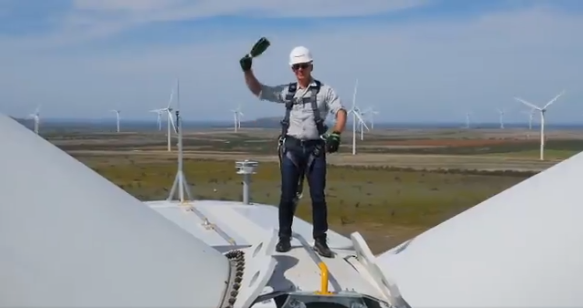 Jeff Bezos holding a champagne bottle on top of a wind turbine